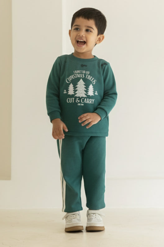 Child wearing a teal outfit with a graphic design, standing in front of a white curtain with small lights.