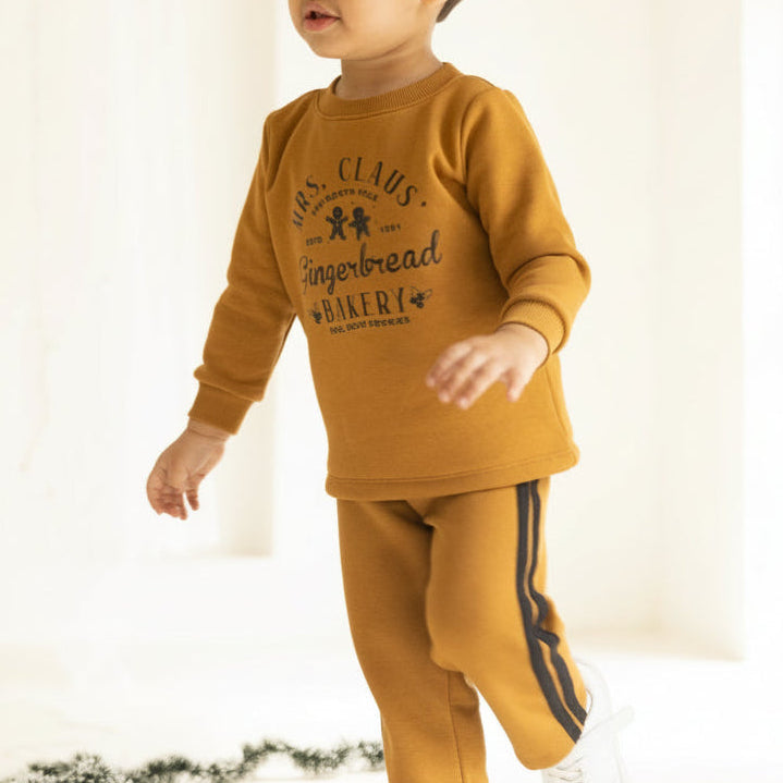 Child wearing a mustard yellow outfit with text, standing indoors on a light background