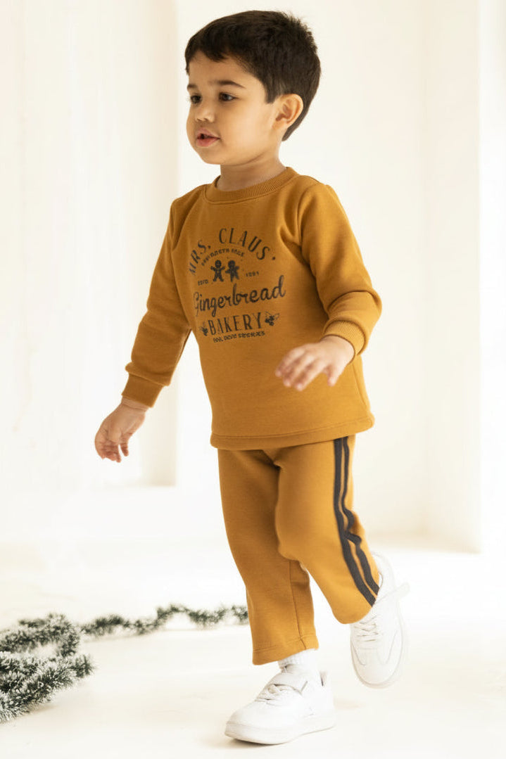 Child wearing a mustard yellow outfit with text, standing indoors on a light background