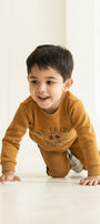 Child in a mustard yellow sweater crawling on a light-colored floor with a neutral background