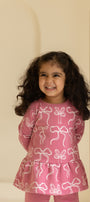Young girl wearing a pink outfit with bow patterns against a beige background