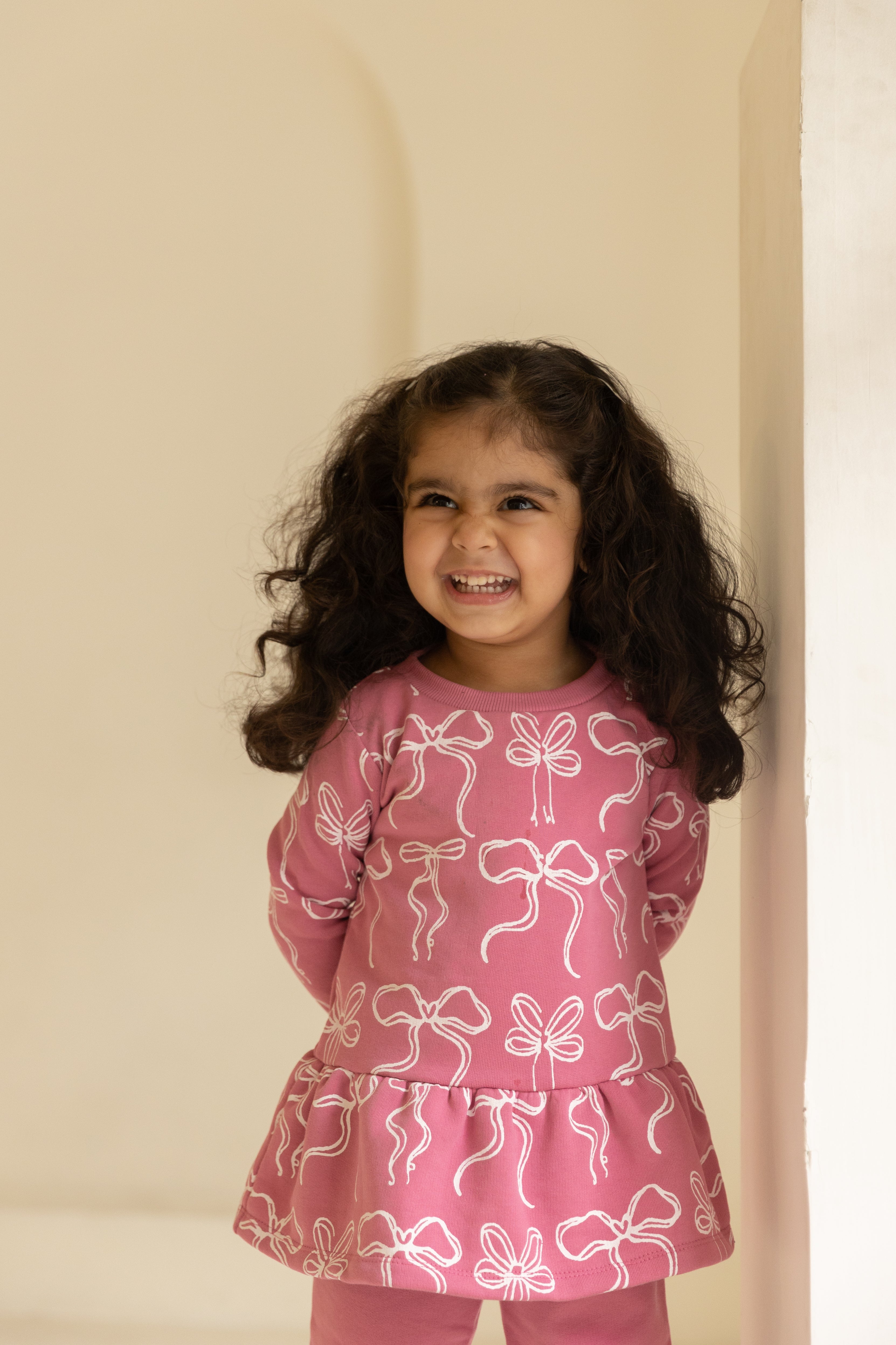 Young girl wearing a pink outfit with bow patterns against a beige background