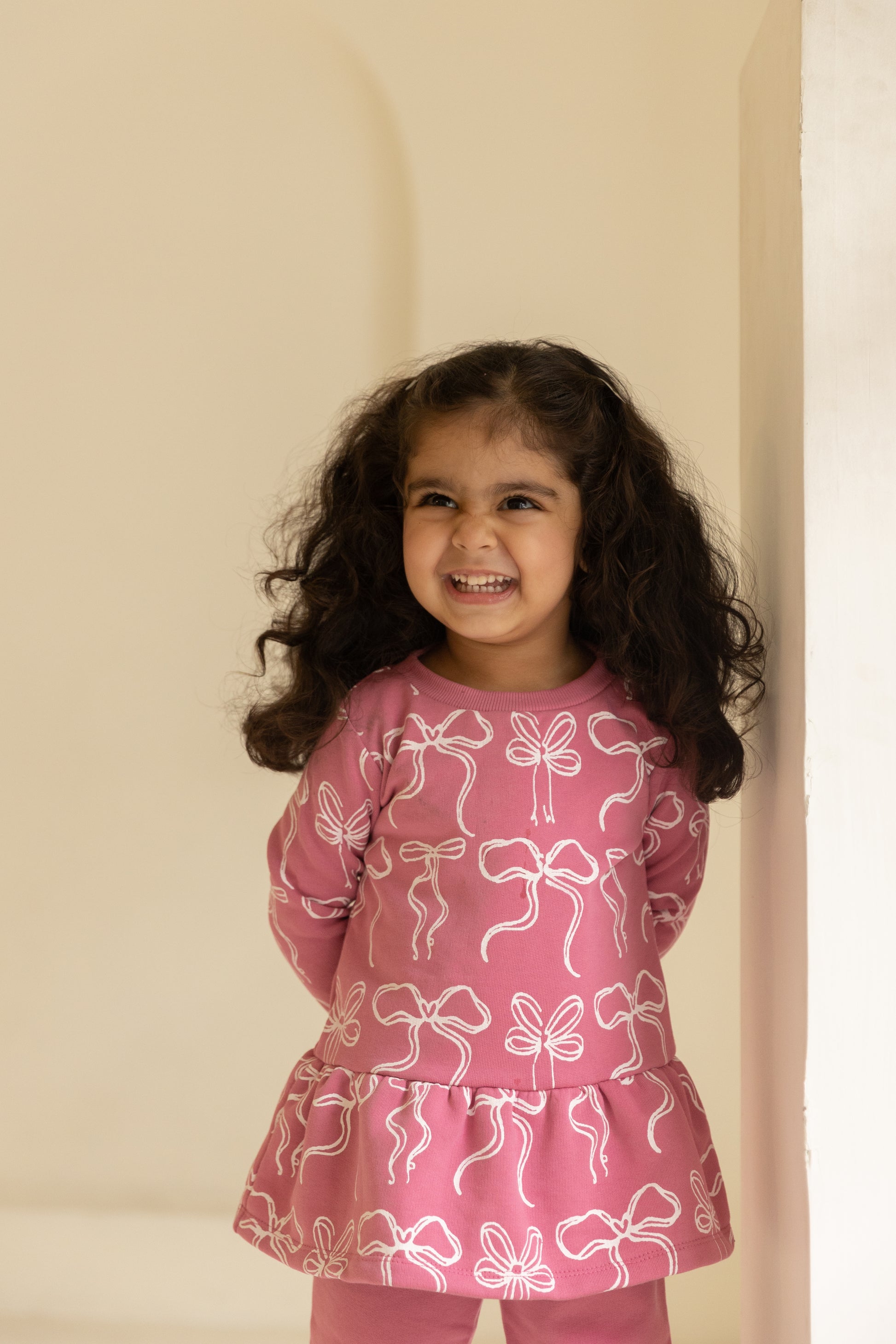 Young girl wearing a pink outfit with bow patterns against a beige background