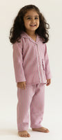 Young girl wearing pink striped pajamas standing against a beige background