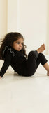 Child in black outfit sitting on a light-colored floor with a neutral wall background wearing AUMORE