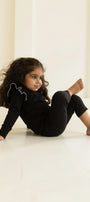 Child in black outfit sitting on a light-colored floor with a neutral wall background wearing AUMORE