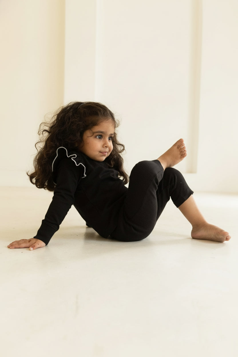 Child in black outfit sitting on a light-colored floor with a neutral wall background wearing AUMORE
