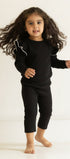 Child wearing a black outfit standing in a minimalistic room with beige walls.