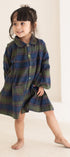 Child wearing a plaid dress standing against a plain background