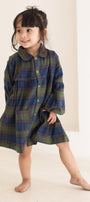 Child wearing a plaid dress standing against a plain background