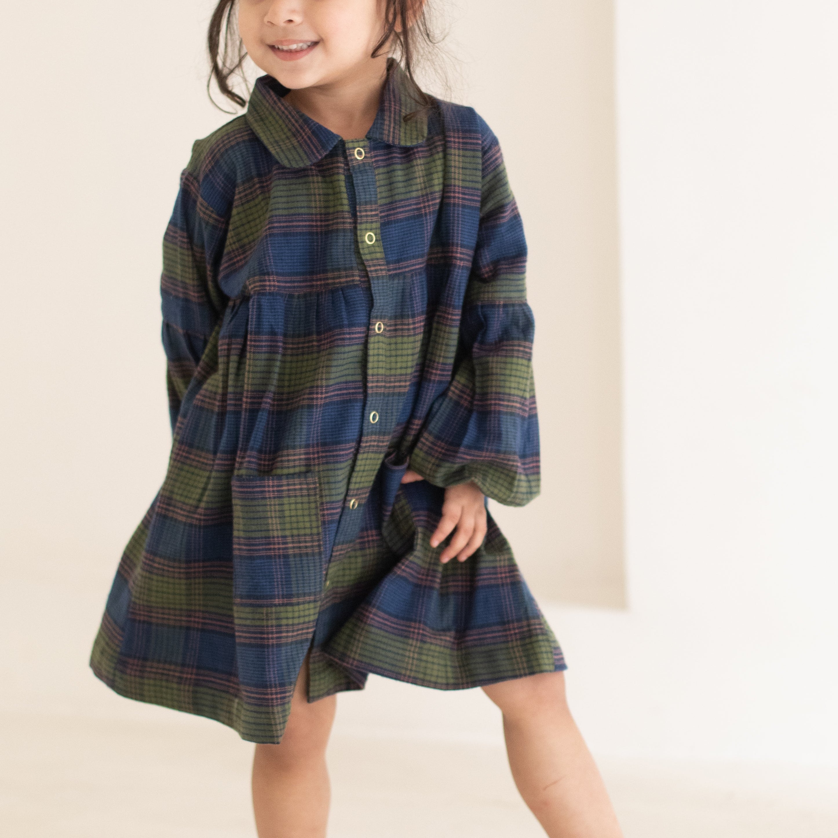 Child wearing a plaid dress standing against a plain background