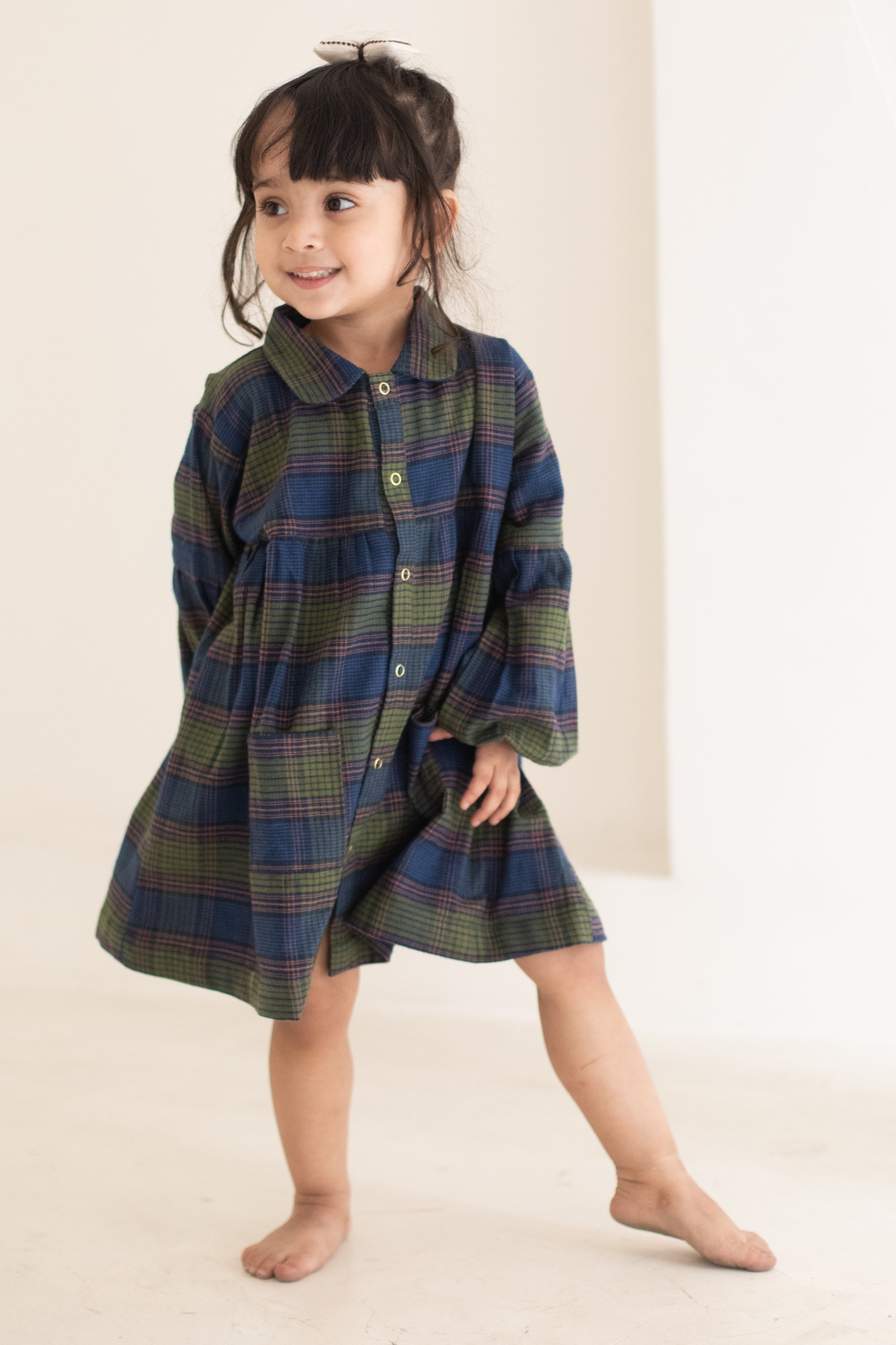 Child wearing a plaid dress standing against a plain background