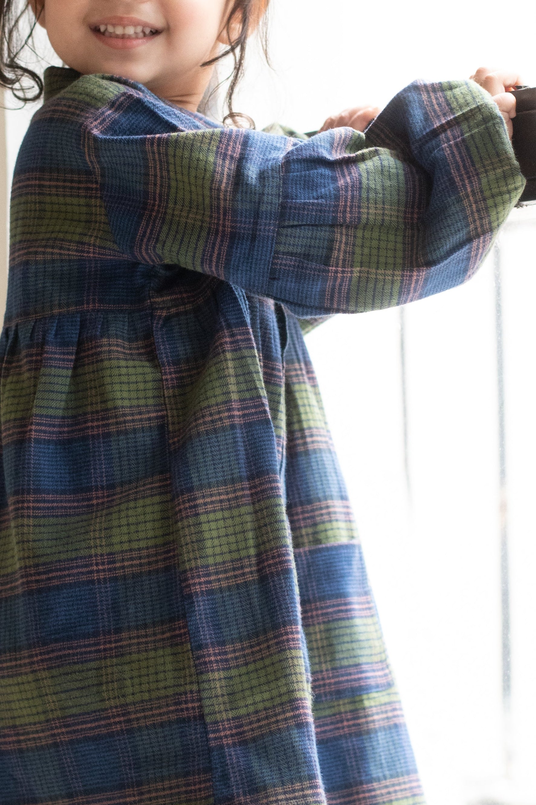 Child wearing a plaid dress standing by a window
