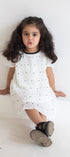 Young girl wearing a white dress with black polka dots on a plain background