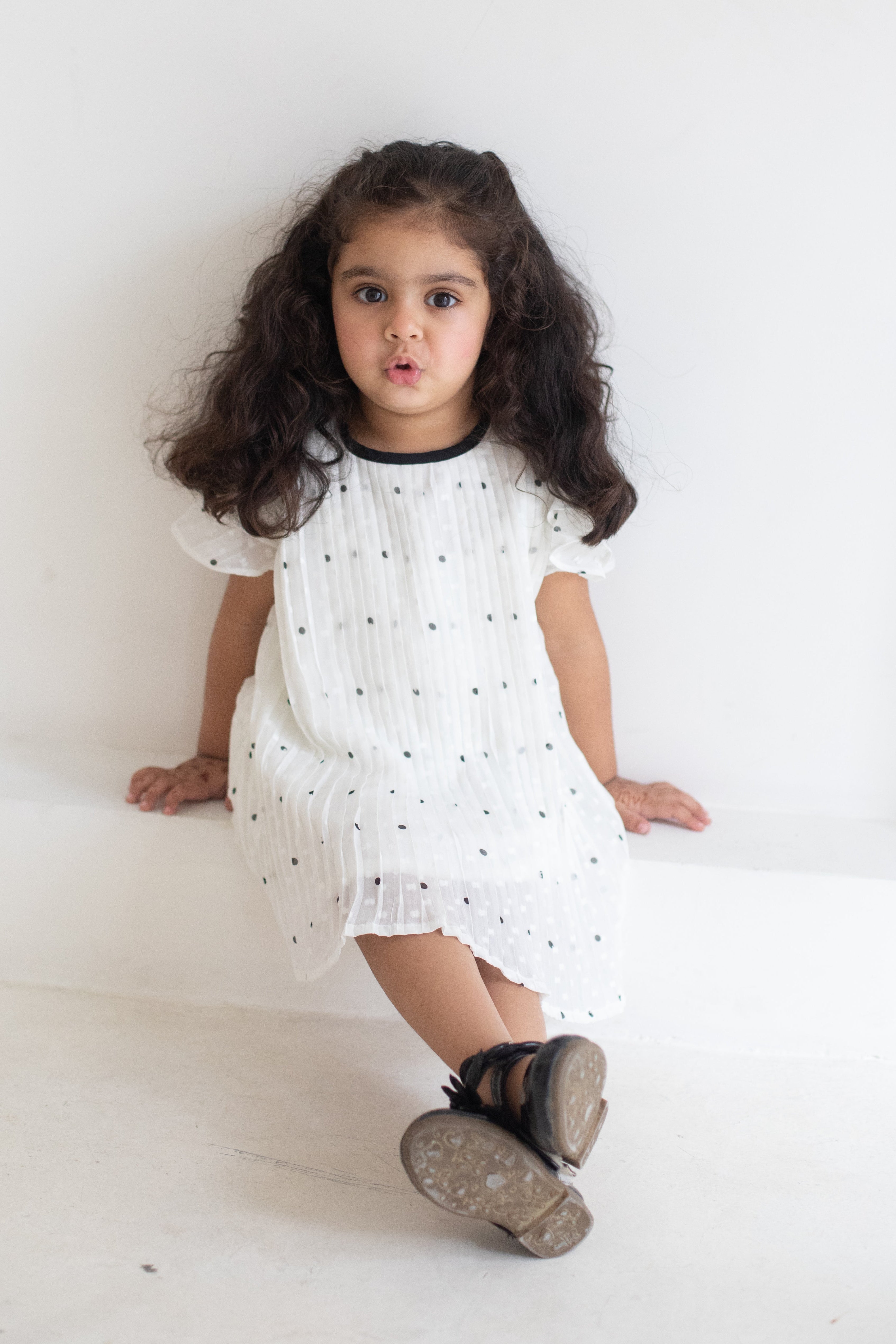 Young girl wearing a white dress with black polka dots on a plain background