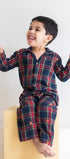 Child wearing a plaid outfit sitting on a yellow block against a white background