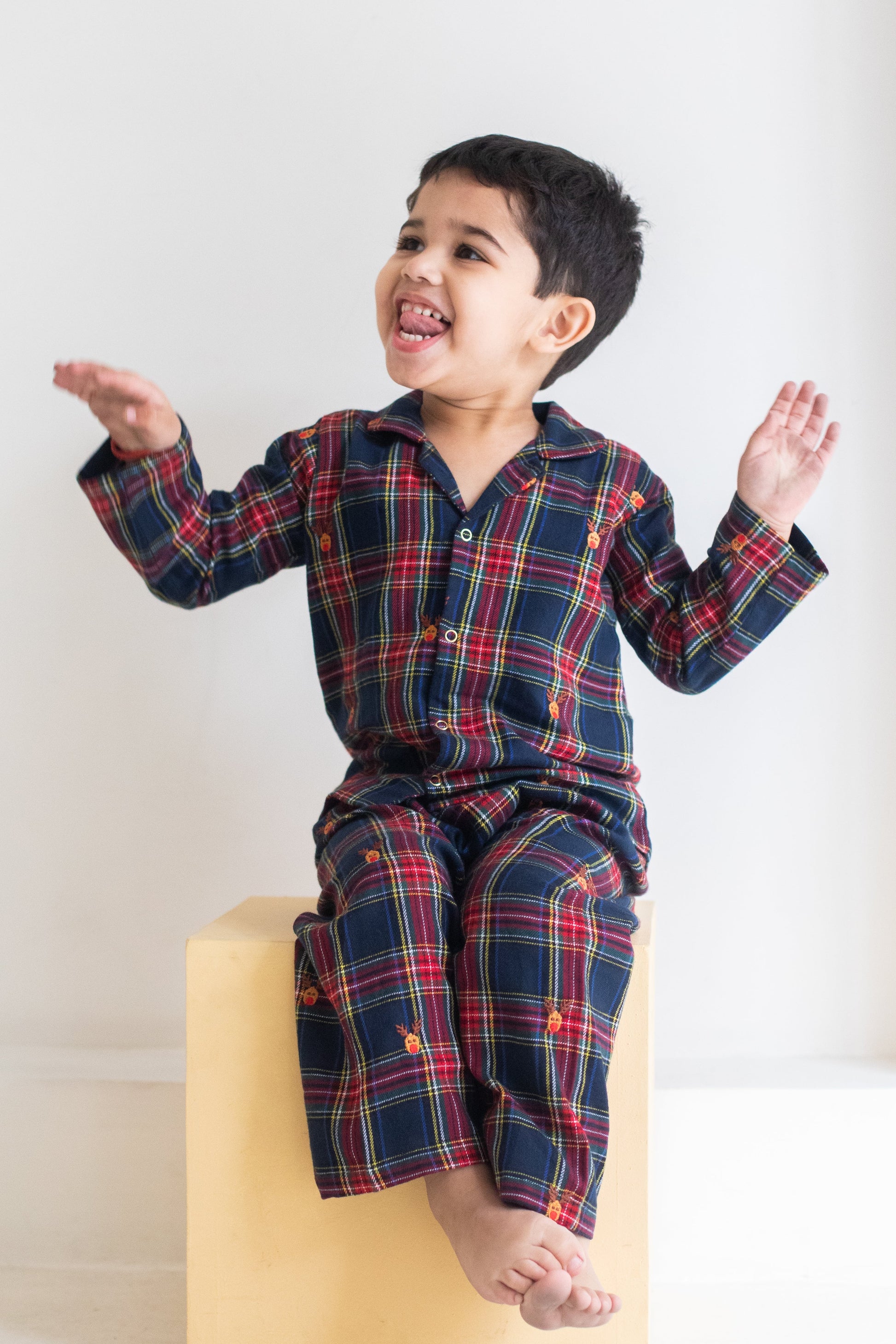 Child wearing a plaid outfit sitting on a yellow block against a white background