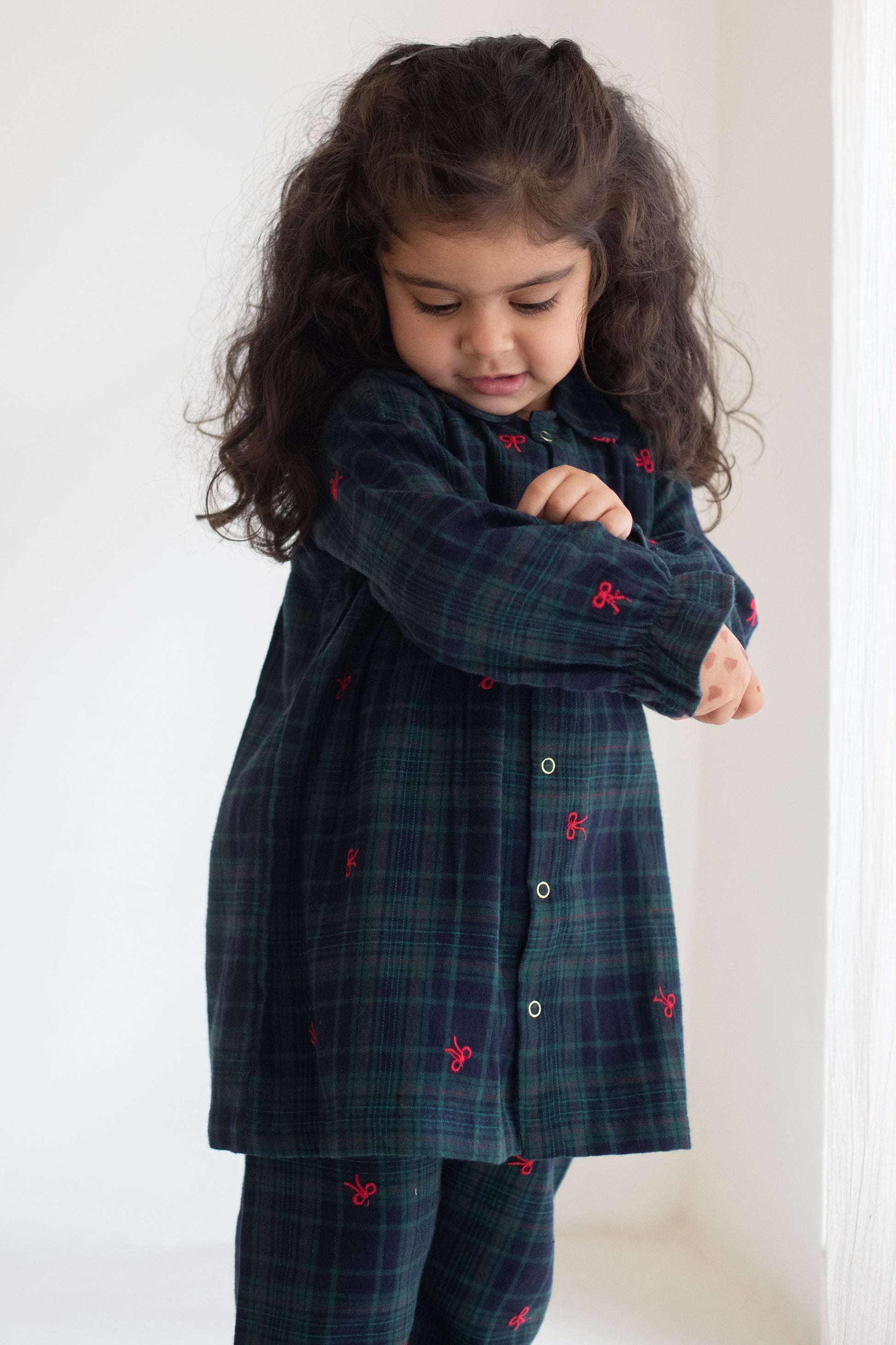 Child wearing a dark blue plaid dress with red accents against a white background