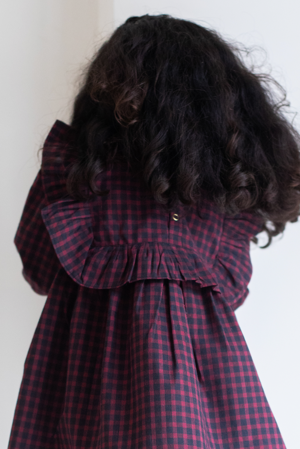Person wearing a red and black checkered dress with long, dark hair.