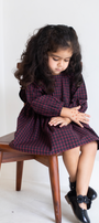 Young girl in a plaid dress sitting on a wooden stool against a white background