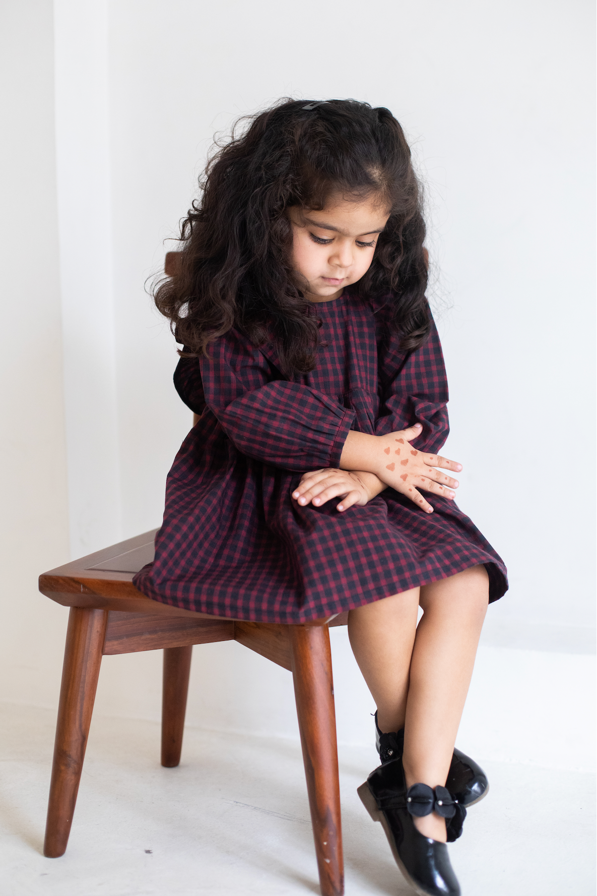 Young girl in a plaid dress sitting on a wooden stool against a white background