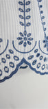 Close-up of a white garment with blue embroidery on a light gray background