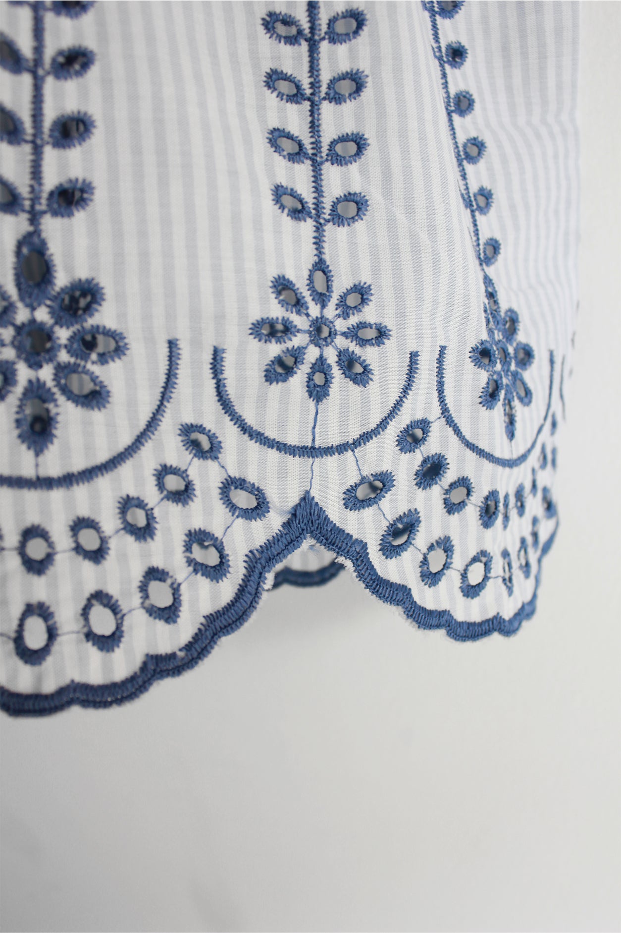 Close-up of a white garment with blue embroidery on a light gray background