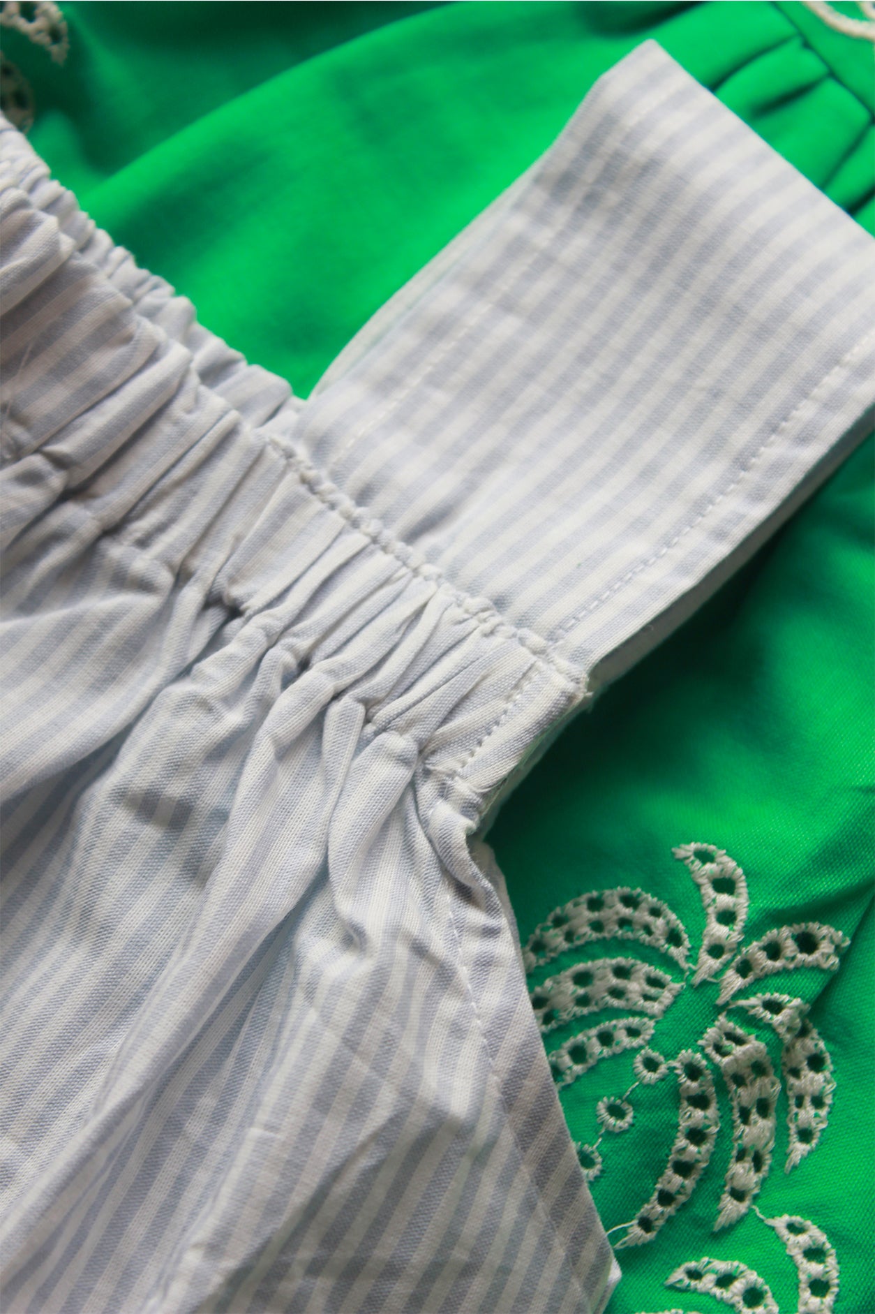 Close-up of a green fabric with intricate silver embroidery and a white striped fabric.
