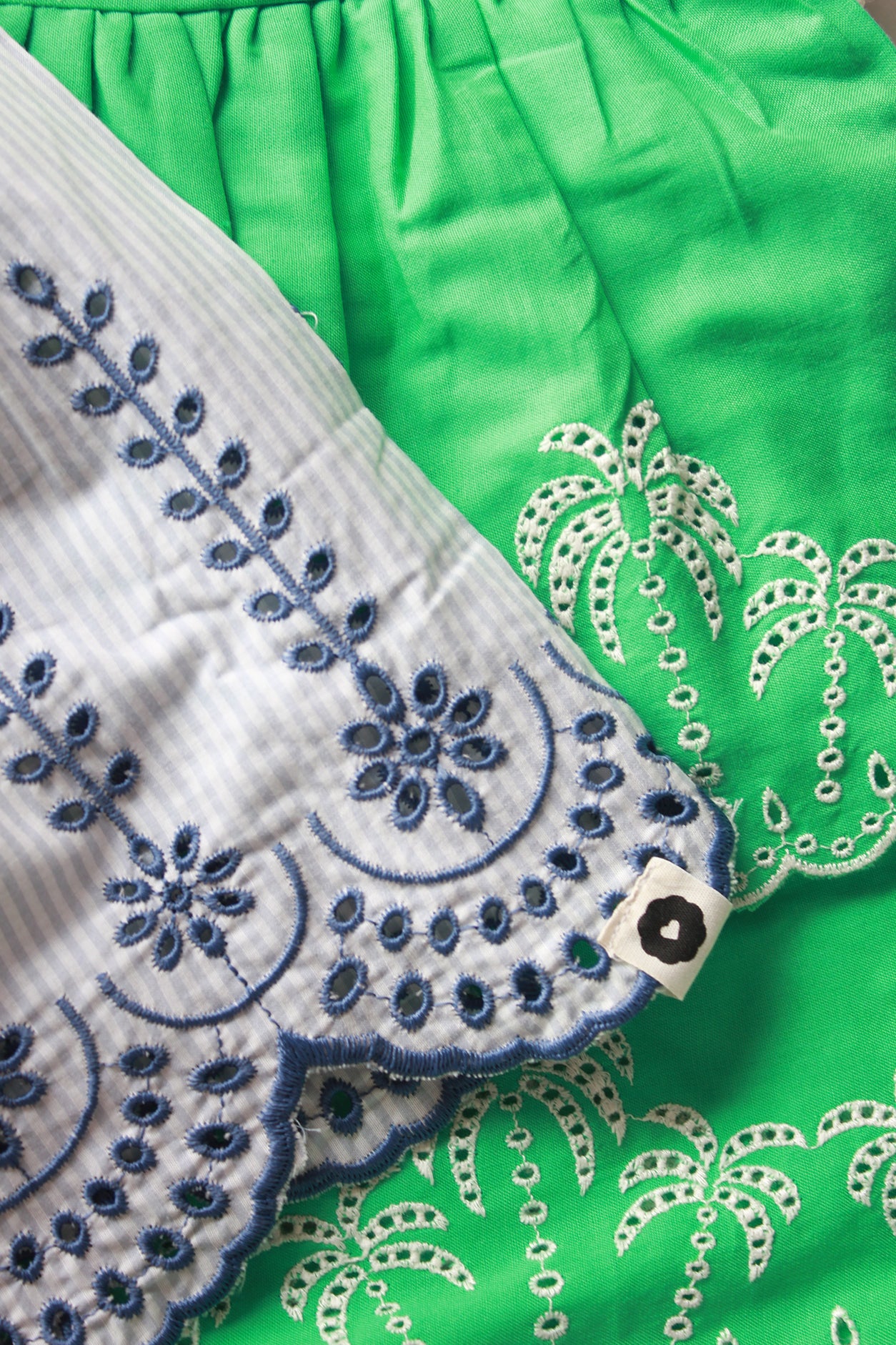 Close-up of green fabric with white embroidery and a white border with blue embroidery.