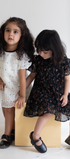 Two young girls in dresses standing on a white floor with a plain background