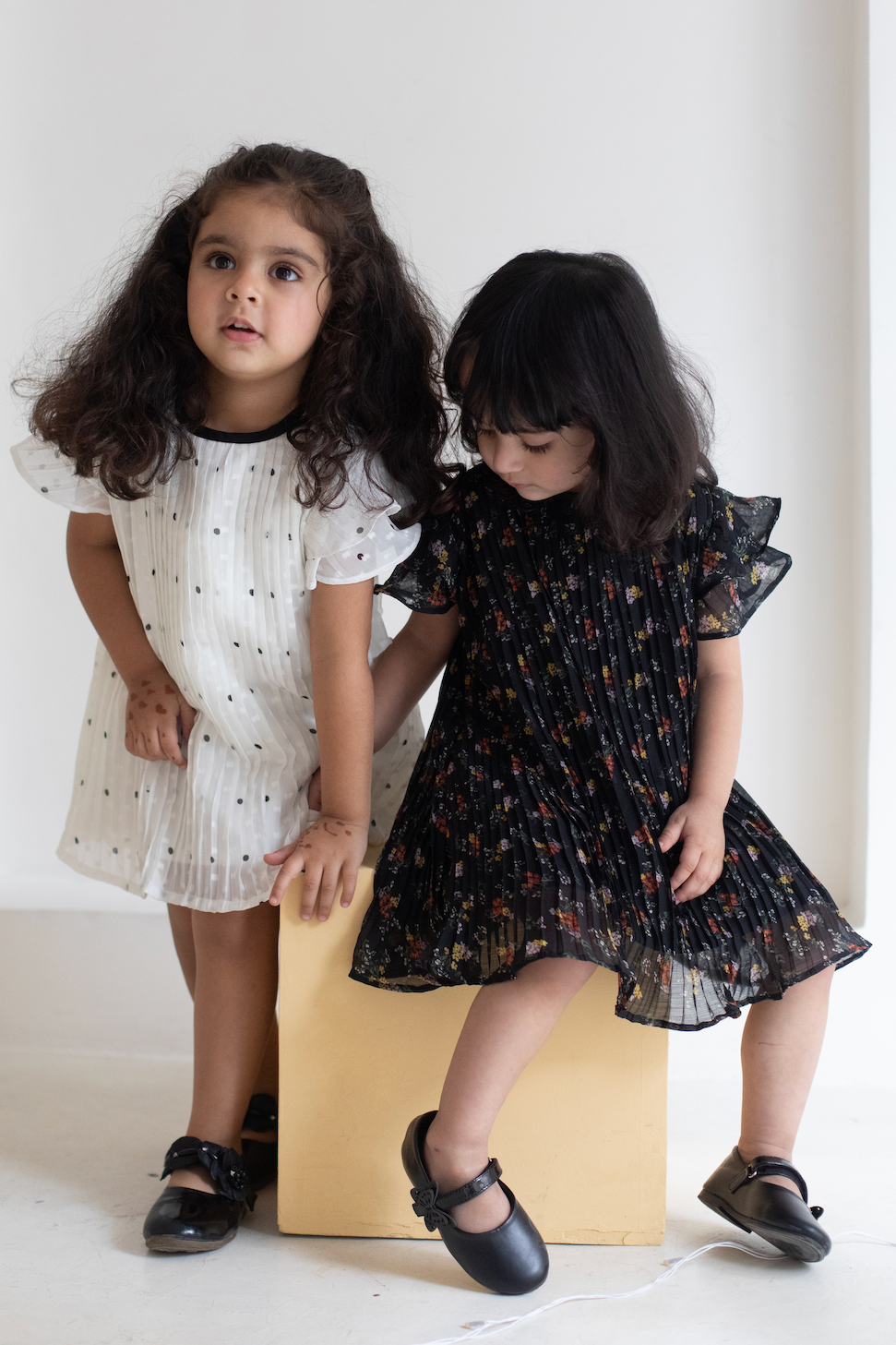 Two young girls in dresses standing on a white floor with a plain background