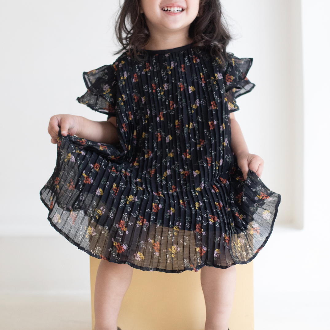 Young girl wearing a black floral dress against a white background