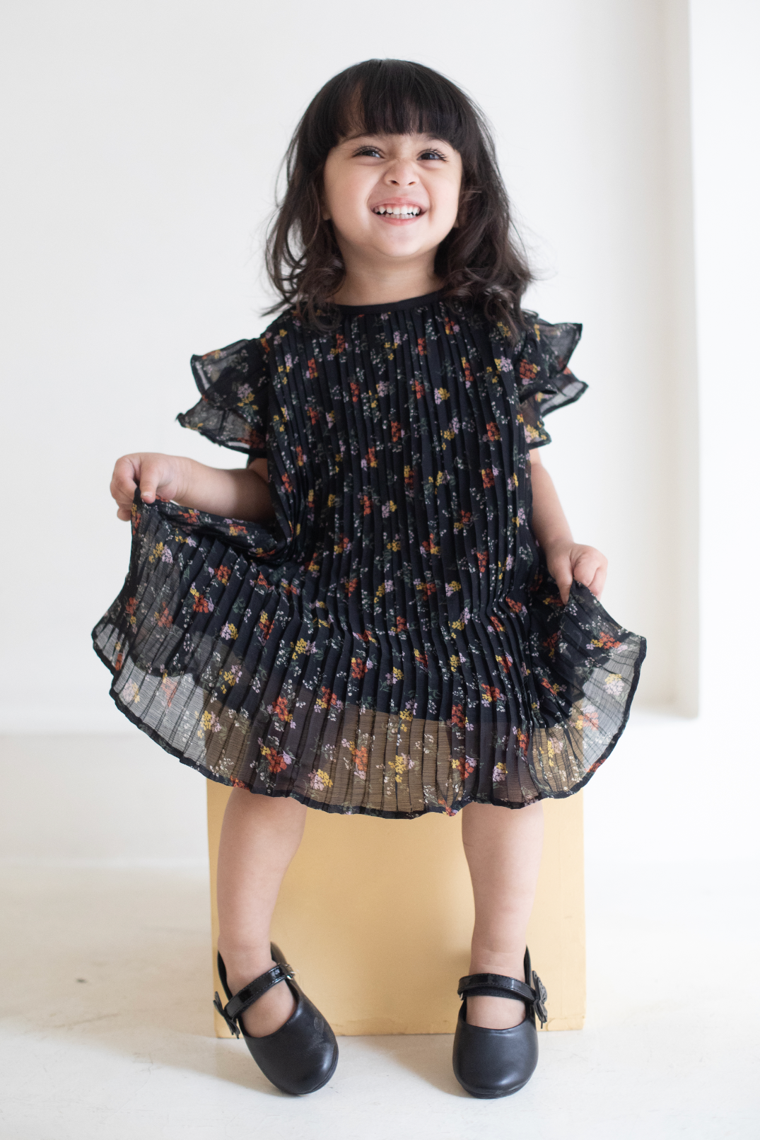 Young girl wearing a black floral dress against a white background