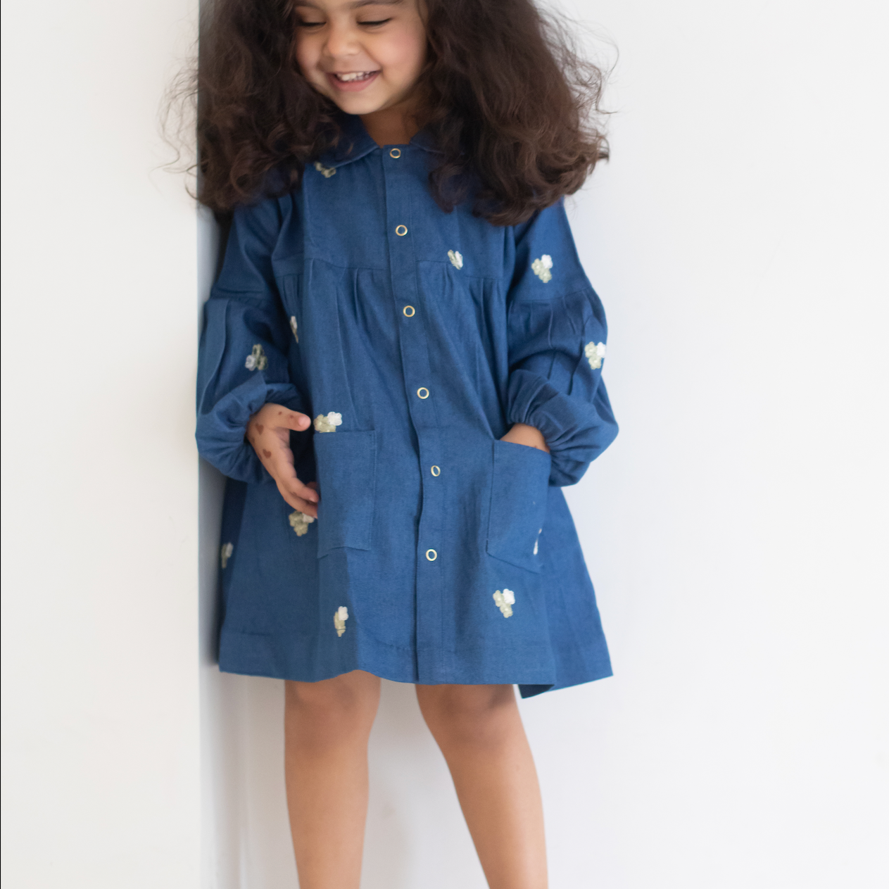 Child wearing a blue dress with white EMRBOIDERED FLOWERS against a white background