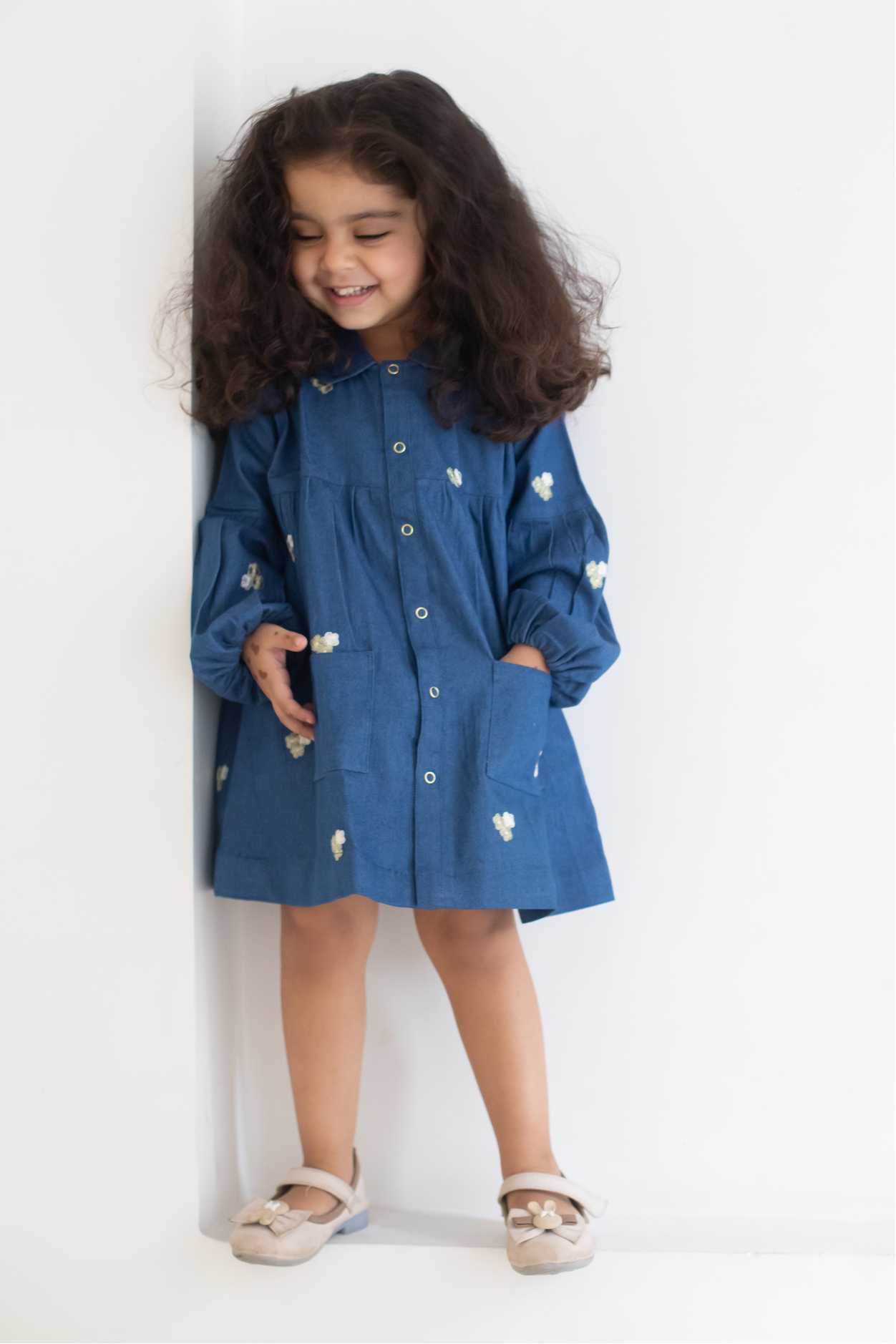 Child wearing a blue dress with white EMRBOIDERED FLOWERS against a white background