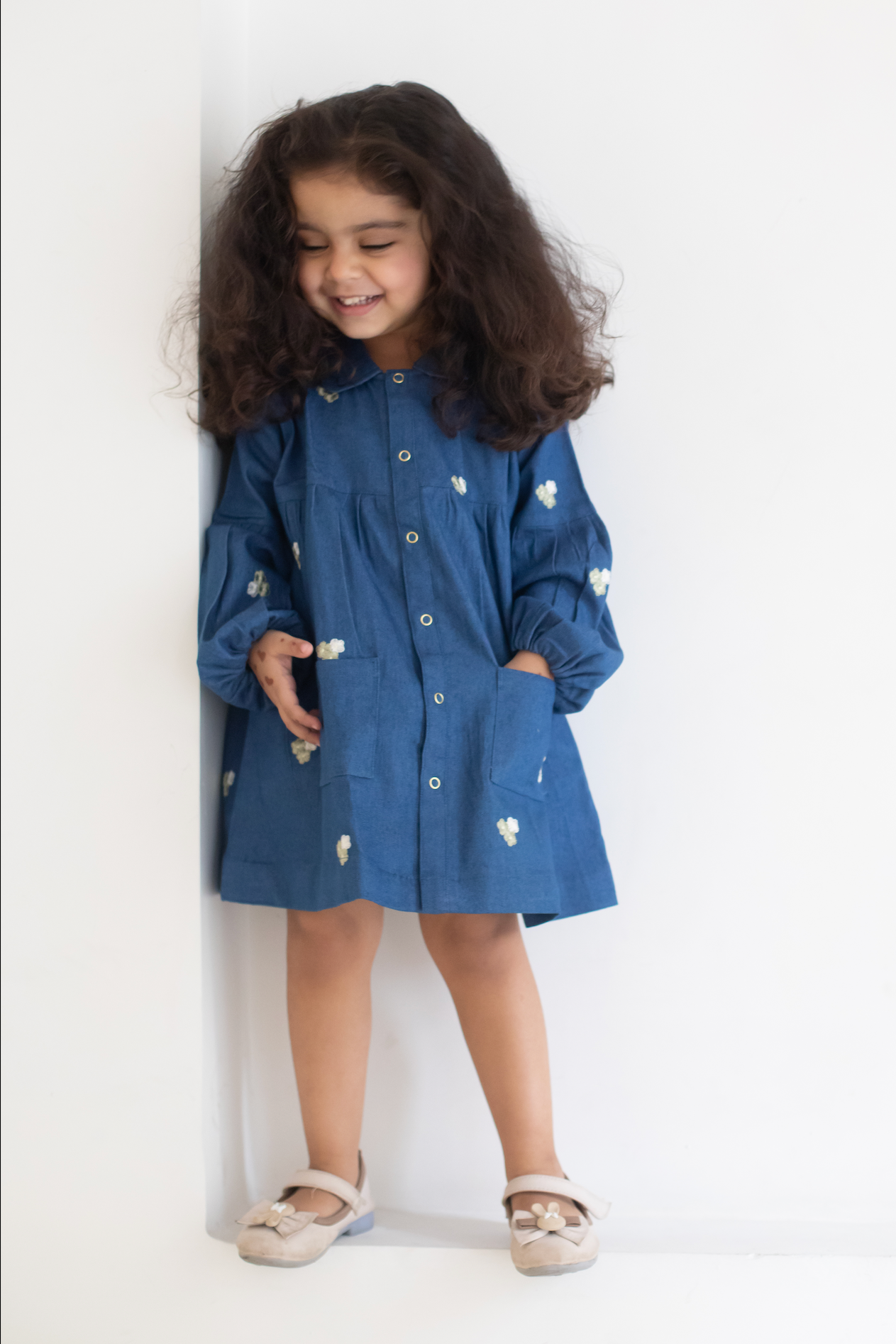 Child wearing a blue dress with white EMRBOIDERED FLOWERS against a white background