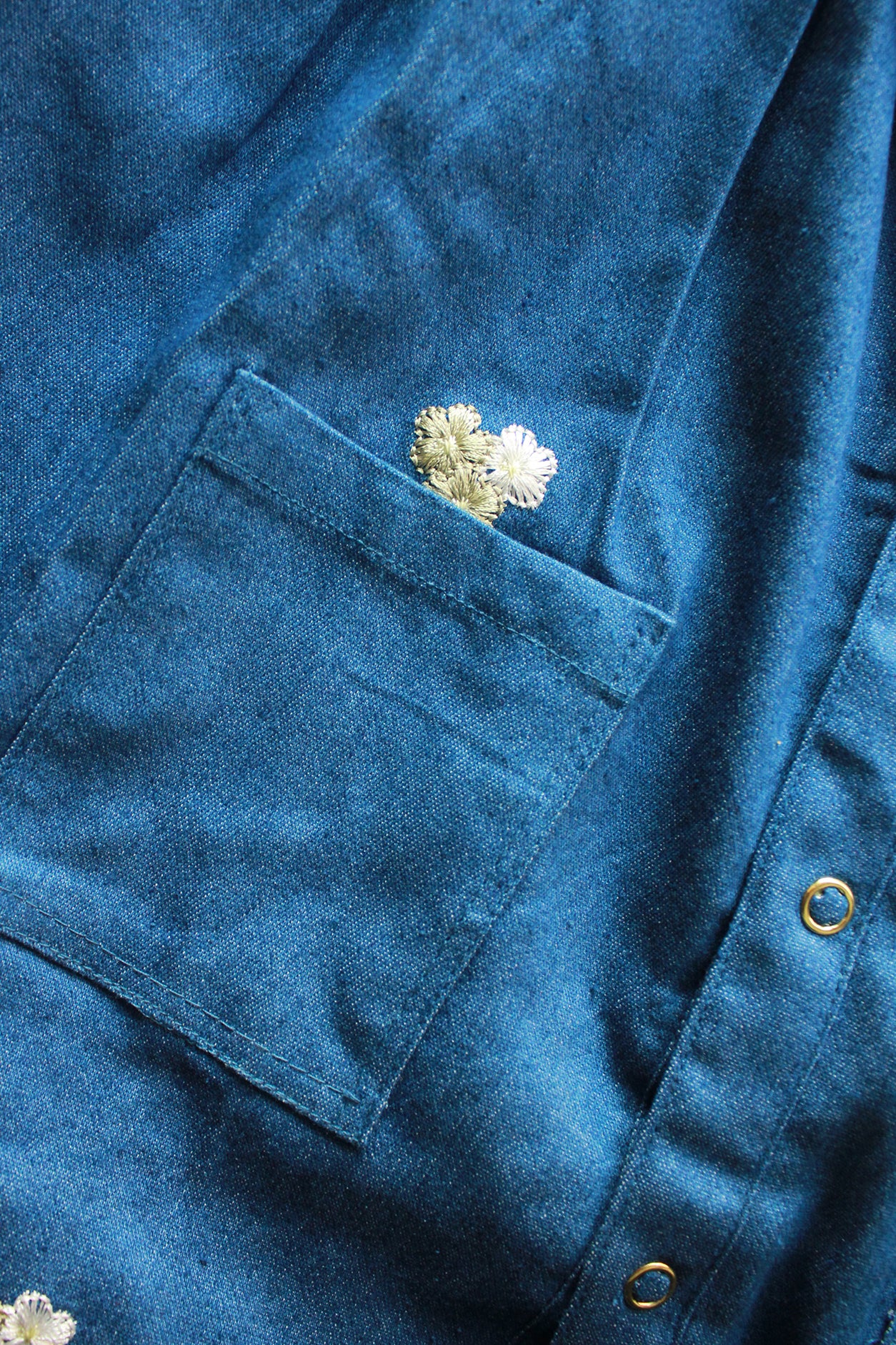 Close-up of a blue jacket with a floral PATCH on the chest pocket.