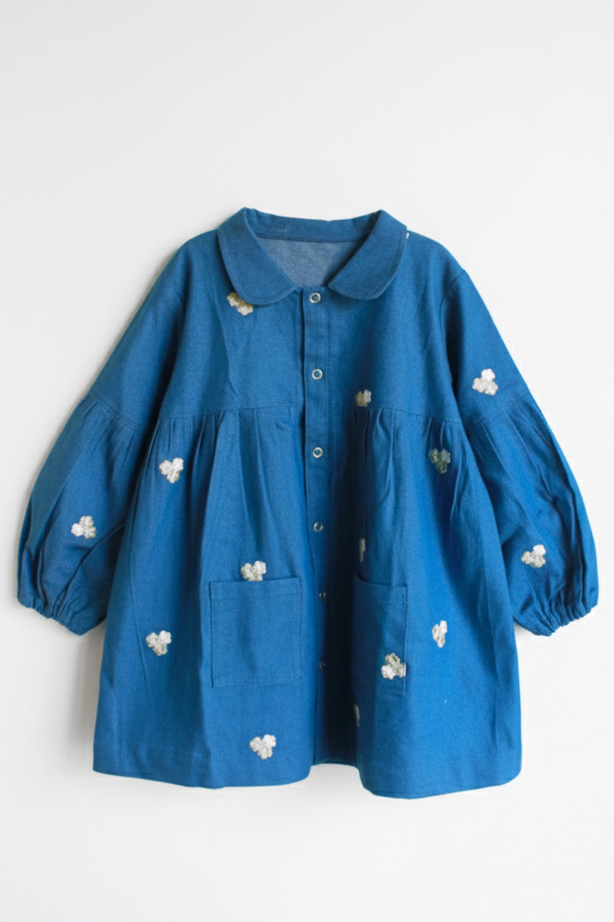 Blue dress with white floral embroidery on a light gray background