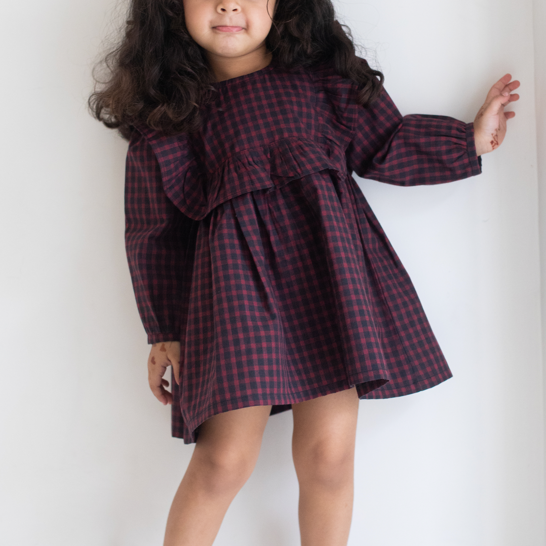 Young girl wearing a red and black checkered dress against a white background
