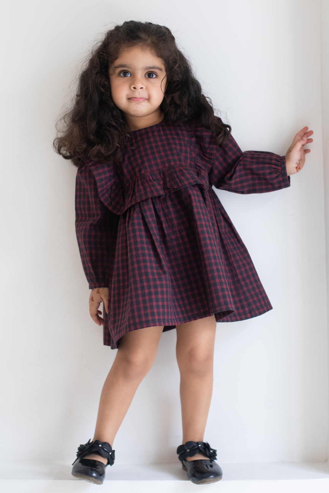 Young girl wearing a red and black checkered dress against a white background