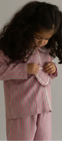 Child wearing a pink and red striped outfit against a beige wall.