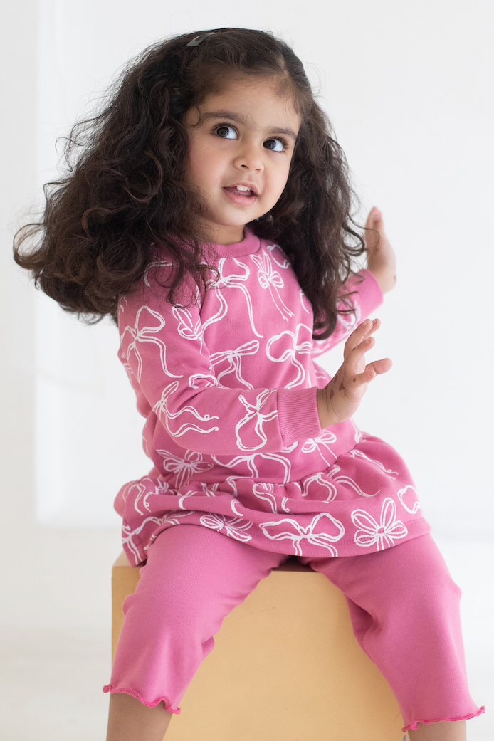Young girl wearing a pink outfit with white patterns on a white background