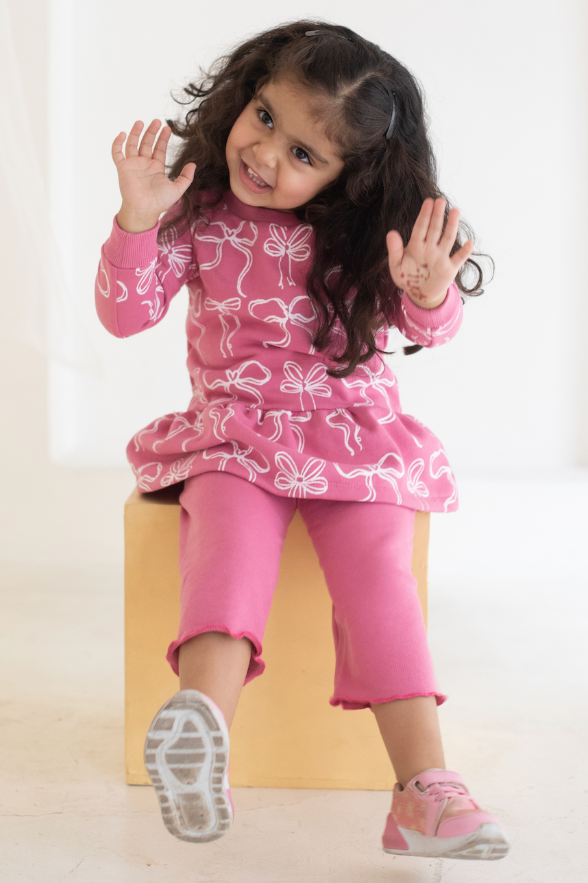 Child in pink  AUMORE outfit with white patterns on a light background