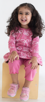 Child wearing an AUMORE KIDS pink outfit with bow patterns sitting on a wooden block against a white background