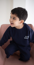 Child wearing a navy blue outfit with text, sitting on a pink chair.