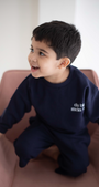 Child wearing a navy blue outfit with text, sitting on a pink chair.