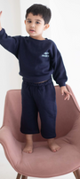 Child wearing a navy blue outfit with 'Chase' text, standing on a pink chair against a white background