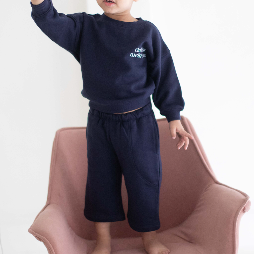 Child wearing a navy blue outfit with 'Chase' text, standing on a pink chair against a white background