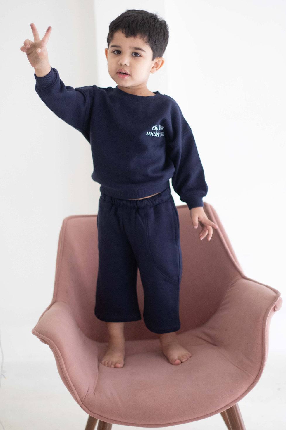 Child wearing a navy blue outfit with 'Chase' text, standing on a pink chair against a white background