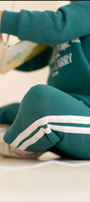 Person wearing a teal tracksuit with white stripes sitting on the floor.